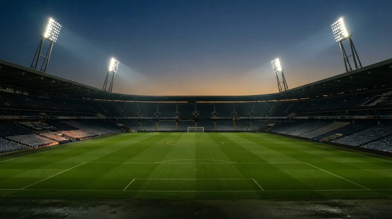 Een leeg voetbalstadion met lichtmasten bij schemering