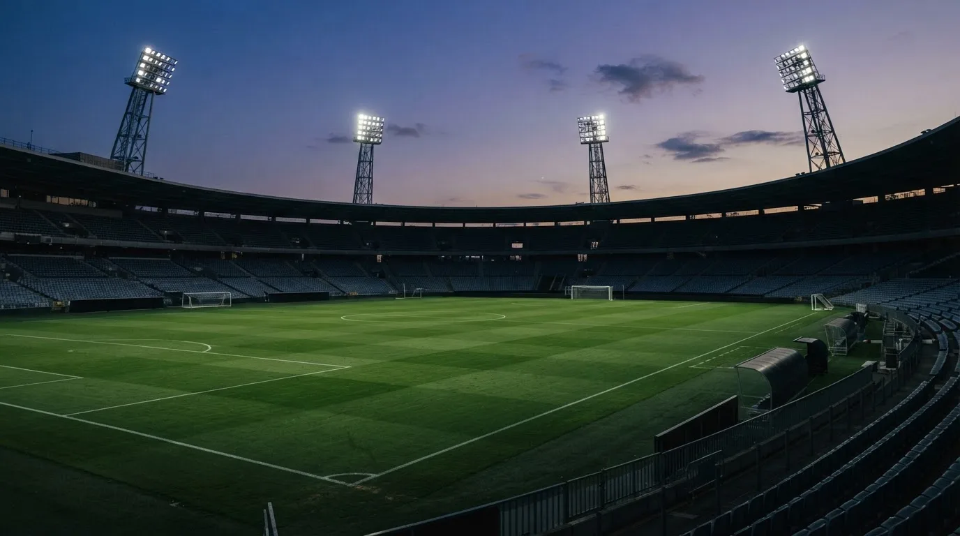 Een leeg voetbalstadion met lichtmasten bij schemering